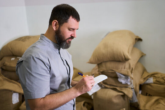 Man in a grey shirt taking notes while surrounded by burlap sacks