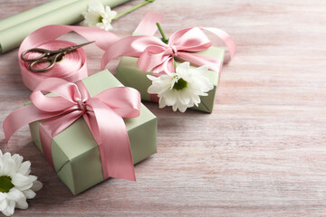 Gift boxes with bows, ribbon, scissors and flowers on pink wooden table, space for text