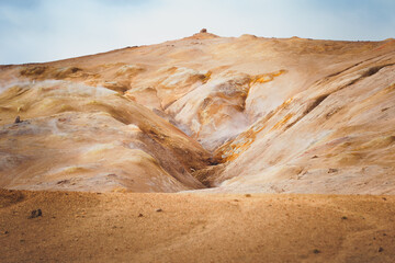 Geothermal terrain with steaming vents, golden-orange soil, and rocky formations near Námafjall, Iceland.