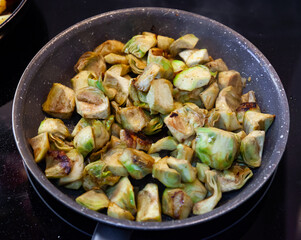 Cooking traditional Catalan vegetarian appetizer of roasted chopped young artichokes on frypan