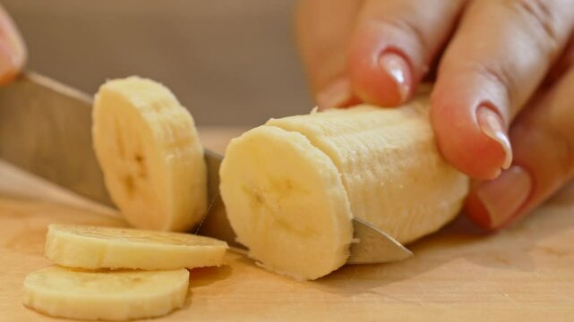 Female hands cutting and slicing yellow banana with knife on wooden board