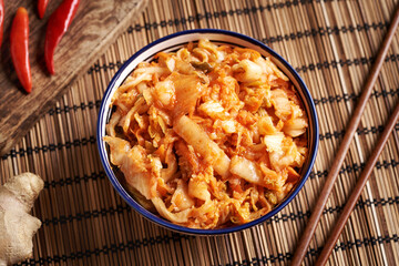 A bowl of fermented kim chi on a table with chilli peppers, ginger and Asian chopsticks