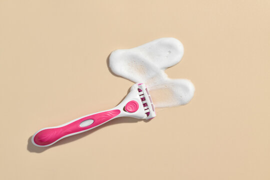 A pink razor with shaving cream on a beige background