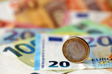One euro coin lies on huge amount of different euro dollars banknotes