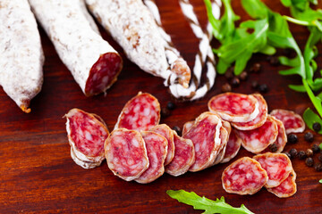 Chopped Spanish sausage fuet on wooden table with arugula and black pepper.