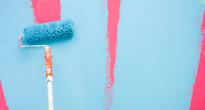 A paint roller is painting with blue and pink colors indoors