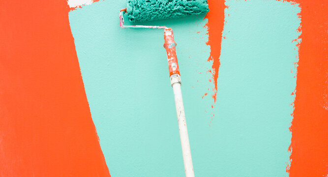 A paint roller is painting with green and orange colors indoors