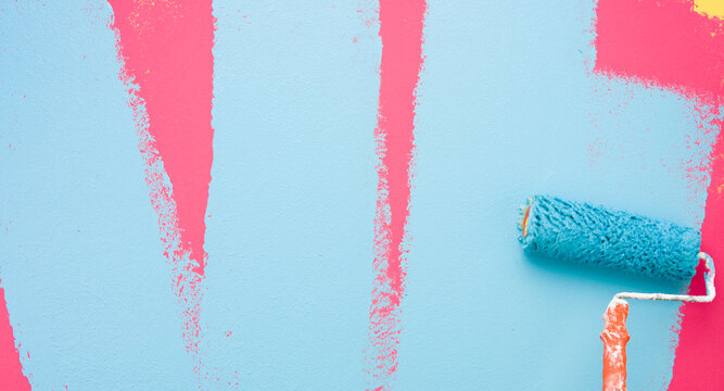A paint roller is painting with blue and pink colors indoors