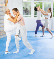 Determined senior woman performing head hold with simultaneous knee strike to midsection of young...