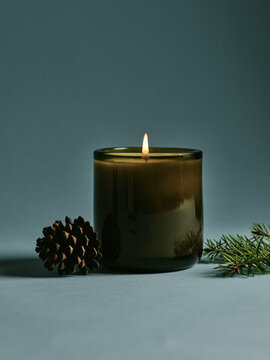 A cozy candle with a pinecone and evergreen sprig on a soft background