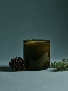 A cozy scented candle beside a pine cone and evergreen sprig