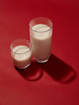 Two glasses of milk against a bright red background