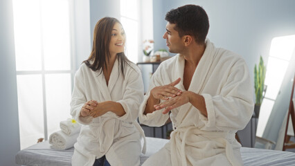 Couple applying lotion in a spa wearing white robes showcasing a relaxed and intimate moment indoors surrounded by wellness decor and natural light