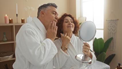 Middle-aged couple in robes at a spa looking into a mirror in a serene wellness center