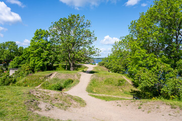 A tranquil pathway winds through lush greenery at Battery Park on Vaxholm Island near Stockholm. Visitors enjoy outdoor activities surrounded by vibrant nature and scenic views of the water.