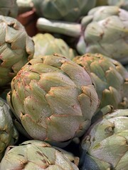 Fototapeta premium Close-up of fresh artichokes displayed in a vibrant farmers market setting. The image captures the natural texture and earthy color of the vegetables, emphasizing organic freshness and healthy eating.