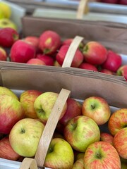 A close-up of vibrant red and green apples displayed in wooden baskets at a market. Represents freshness, autumn, harvest, and healthy eating.