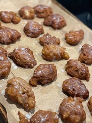 Freshly baked apple fritters with a sweet glaze, cooling on a parchment-lined baking sheet. Perfect for breakfast or dessert, these treats offer a delicious blend of flavors and textures.