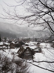 Snow-covered traditional Gassho-style village in Shirakawa-go, Japan, surrounded by misty mountains.