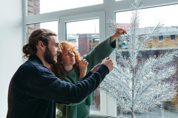 Couple Decorating a Silver Christmas Tree Indoors
