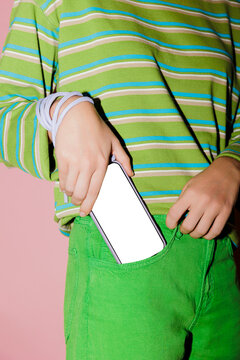 Woman putting smartphone with blank screen in green jeans pocket
