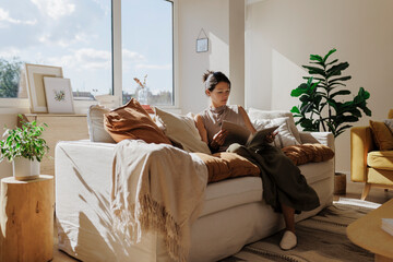 Woman reading a magazine on a comfortable sofa in a sunny living room