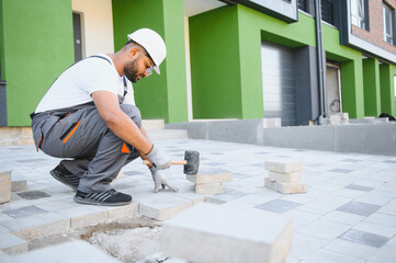 Indian worker lay paving tiles, construction of brick pavement, men's hands in gloves.