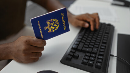 Close-up of young man holding a cuban passport while working at a computer in an office setting,...