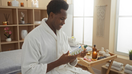 Young african american man in a spa wearing a white robe, examining a product bottle in a tranquil wellness center with soothing decor