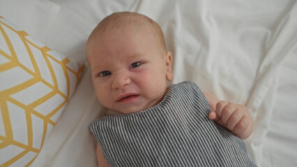 Newborn boy lying on bed in bedroom at home with striped clothing and yellow patterned pillow