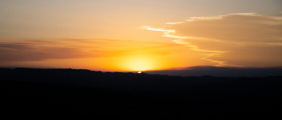 The warm hues of a summer sunset blend beautifully as the sun dips below the horizon. Silhouettes of hills create a serene backdrop, highlighting the tranquility of the evening sky.