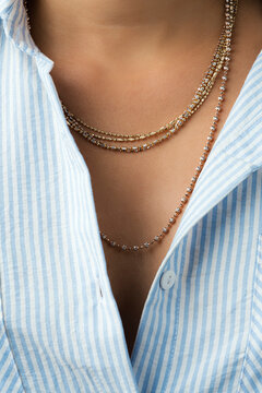 Layered gold chains seen between blue and white striped shirt