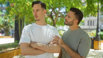 Gay couple arguing in an urban park with one man comforting another during a discussion on a sunny day
