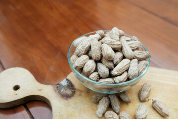 Organic Raw Peanuts in a glass Bowl on wooden cutting board in the wooden table, healthy snack