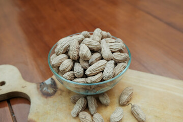 Organic Raw Peanuts in a glass Bowl on wooden cutting board in the wooden table, healthy snack