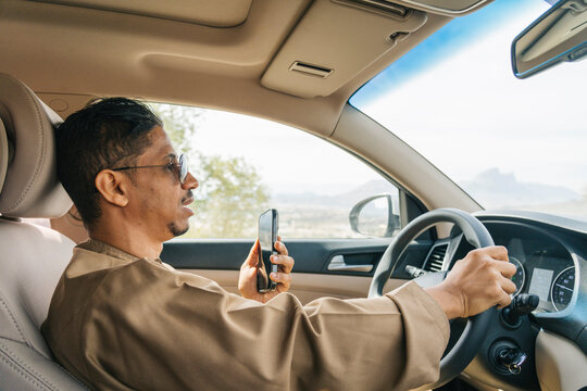 Arab man driving car while using smartphone:
