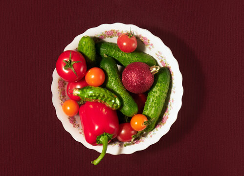 Plate with vegetables and Christmas tree toys on textured red backdrop