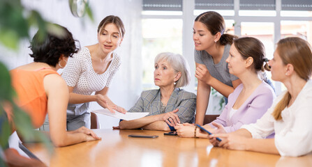 Women of different ages examine documents while sitting at table in office