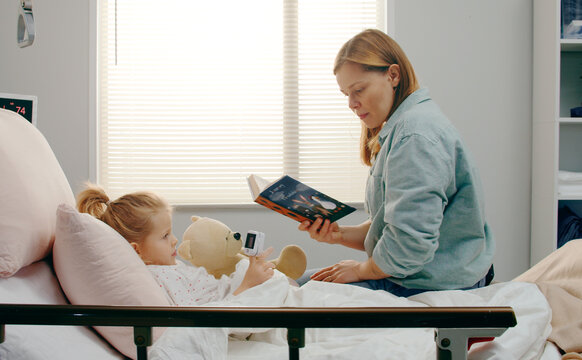 Mother reading book to sick daughter in hospital bed