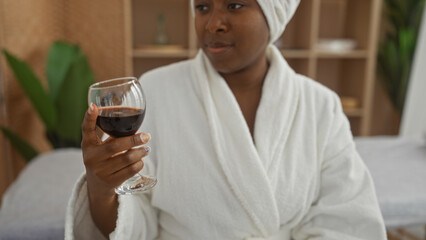 Woman relaxing in spa holding a glass of wine in a wellness room wearing a bathrobe with indoor plants in background