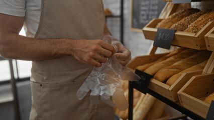 Man wearing a beige apron preparing to work in a bakery with an assortment of fresh bread displayed in wooden racks inside the shop