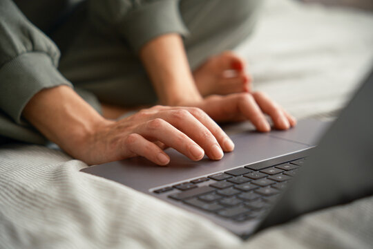 Crop of woman using laptop in bed