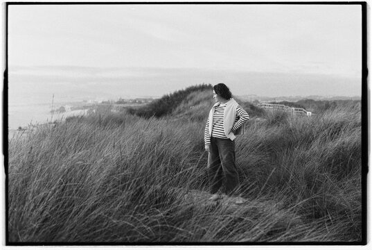 Woman standing in tall grass on a coastal dune with a serene bac