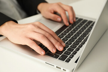 Businesswoman using laptop at white table indoors, closeup. Modern technology