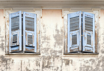 Old weathered house facade with two blue shuttered windows