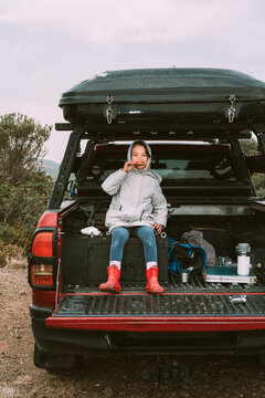 Little girl sitting at the back of a pickup truck, eating a snack