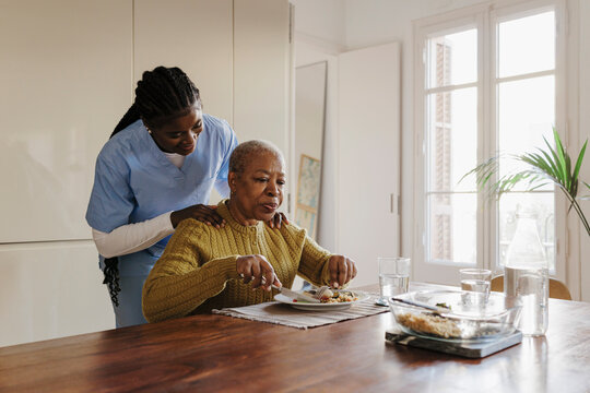 Nurse assisting elderly woman eating lunch at home