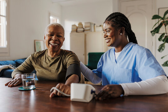 Nurse checking blood pressure of happy senior woman at home