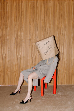 Person with Paper Bag Head Sitting on Red Chair
