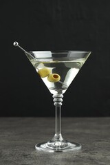 Martini cocktail with olives in glass on grey table against black background
